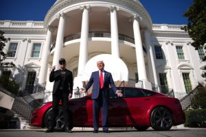 Two people standing outside a red car in front of a building resembling the White House
