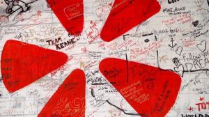 Wall covered in various handwritten messages, signatures, and drawings with red triangular shapes resembling Yelp logo