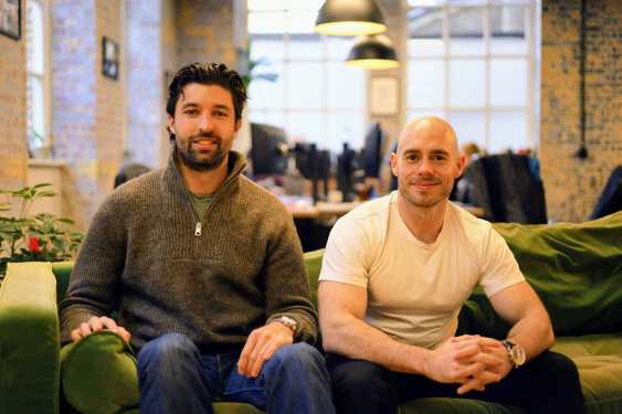 Two men sitting on a green couch in an office setting