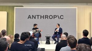 Two individuals seated on stage discussing at a formal event with the logo ANTHROPIC displayed in the background