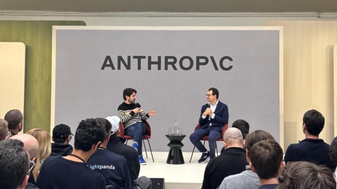 Two individuals seated on stage discussing at a formal event with the logo ANTHROPIC displayed in the background