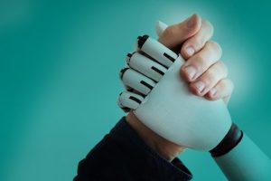 A human hand shaking hands with a robotic or prosthetic hand against a teal background, symbolizing collaboration in a robot-driven world.