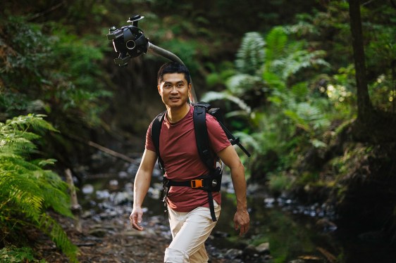Person walking through a lush forest with a camera on a stabilizer rig, illustrating innovative use of AI in outdoor video capturing