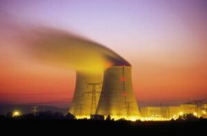 Cooling towers of a nuclear power plant emitting steam during sunset with colorful sky and power lines in the foreground, symbolizing advancements in nuclear power technology.