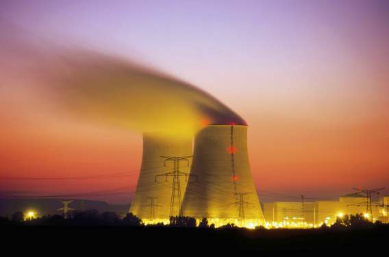 Cooling towers of a nuclear power plant emitting steam during sunset with colorful sky and power lines in the foreground, symbolizing advancements in nuclear power technology.