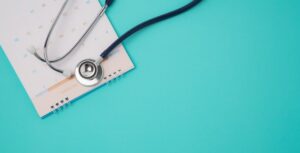 Stethoscope placed on an open calendar against a turquoise background, symbolizing health and awareness related to AI and personal health stories