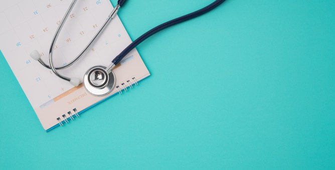 Stethoscope placed on an open calendar against a turquoise background, symbolizing health and awareness related to AI and personal health stories