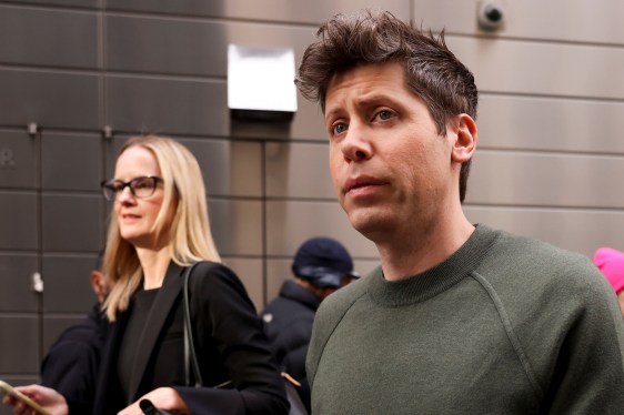 Two people walking outdoors in an urban area, one wearing a green sweater and the other with glasses and a black outfit, with buildings in the background, representing future AI advancements.