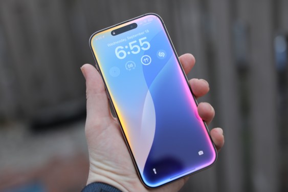 Person holding smartphone with the time 6:55 and colorful background, highlighting delays in AI-powered Siri update