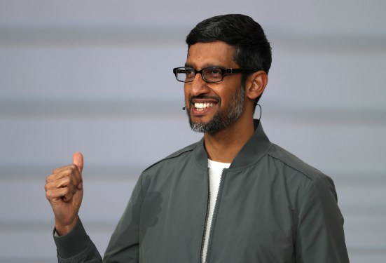 Sundar Pichai wearing glasses and a gray jacket, smiling and giving a thumbs-up during a speech or event related to growth plans